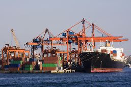 A panoramic view of port activities: containers, cranes, and a moored boat.