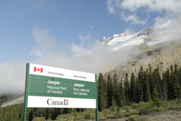 Vue panoramique d'une partie du parc national de Jasper avec, en premier plan, la pancarte autoroutière annonçant l'entrée dans le parc.