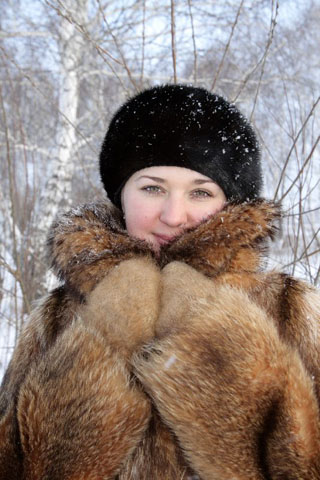 A woman wearing a fur coat and a hat looks at the camera. 