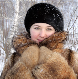A woman wearing a fur coat and a hat looks at the camera. 