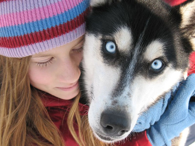 Close-up of a young girl embracing the head of a dog staring at the camera. 