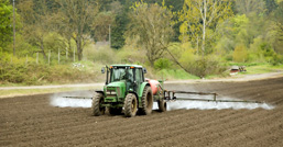 Un tracteur roule dans un champ labouré et procède à l'épandage de produits chimiques.
