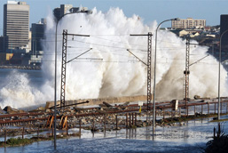 A gigantic wave dramatically hits the coastline of an industrialized city. 