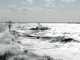 A panoramic view of a wild sea with waves submerging a pontoon.