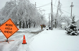 Paysage hivernal avec des arbres et des poteaux électriques givrés, de même qu'une route glacée sur laquelle un panneau de signalisation orangé annonce la tenue de travaux.