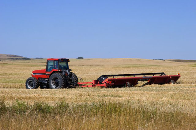 Un tracteur vu de profil procède à la coupe des foins dans un champ cultivé.