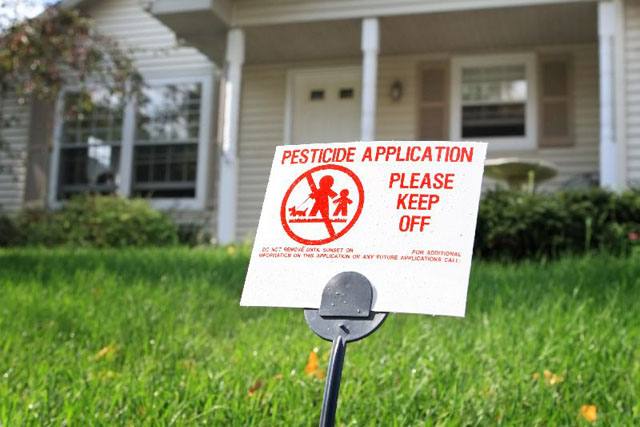 Small sign standing on a lawn informing of the spraying of pesticides. 